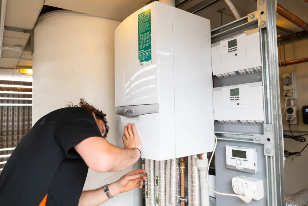 Technician servicing a wall mounted heat pump unit in a plant cupboard