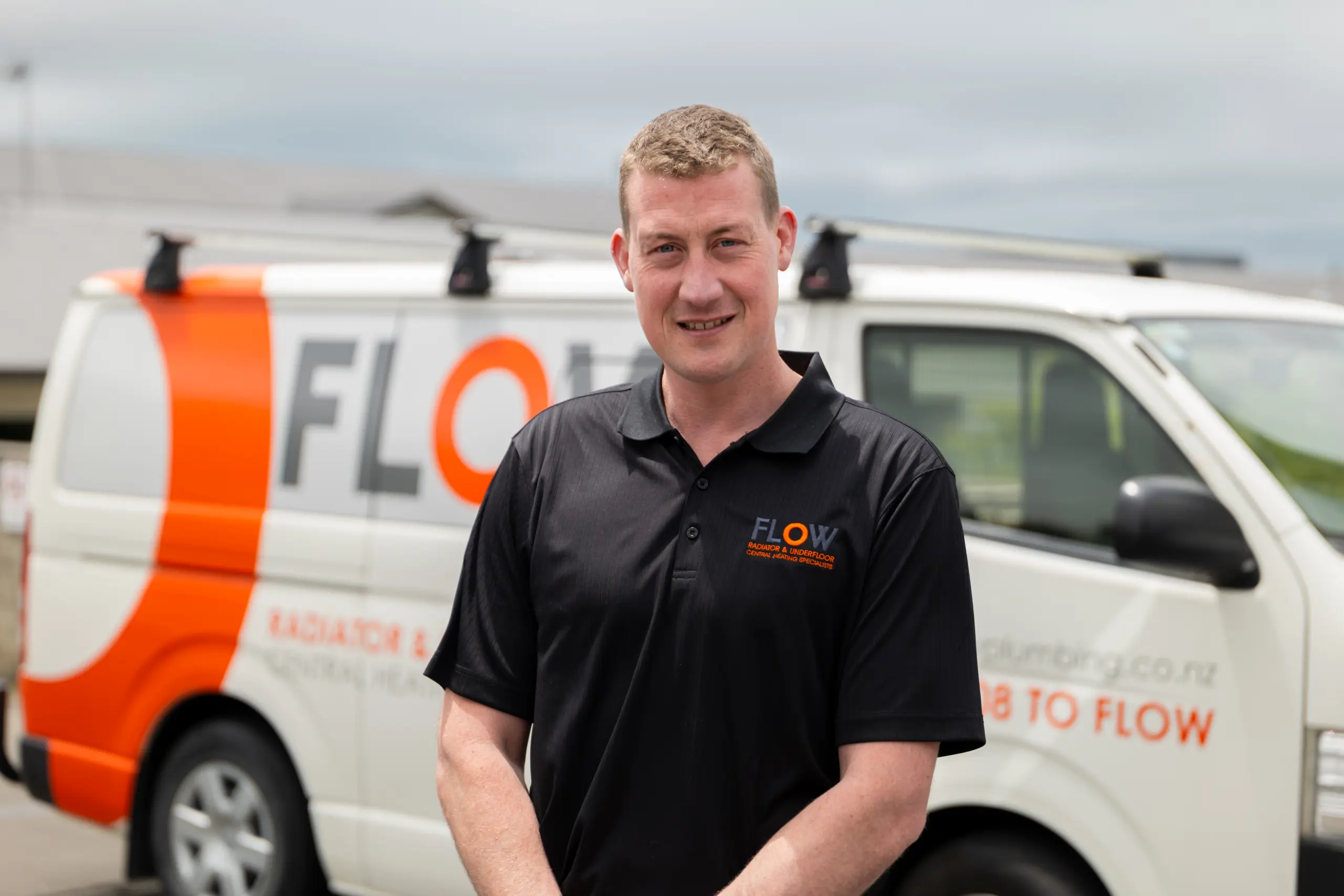 Flow Heating team member in uniform beside a branded van